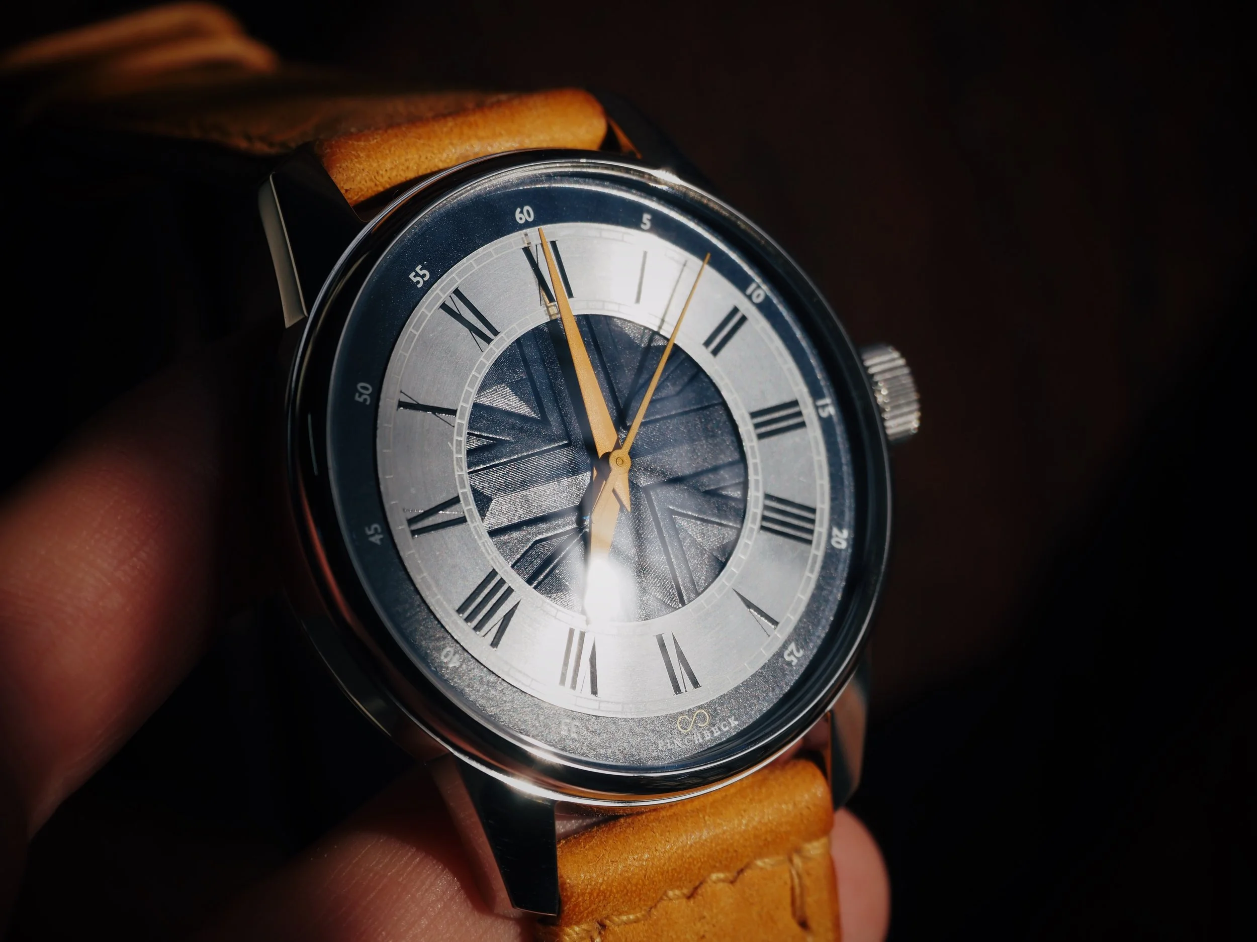 Close-up of a Harold Pinchbeck luxury Blue Albion wristwatch with a silver and blue face, Roman numerals, and a tan leather strap.