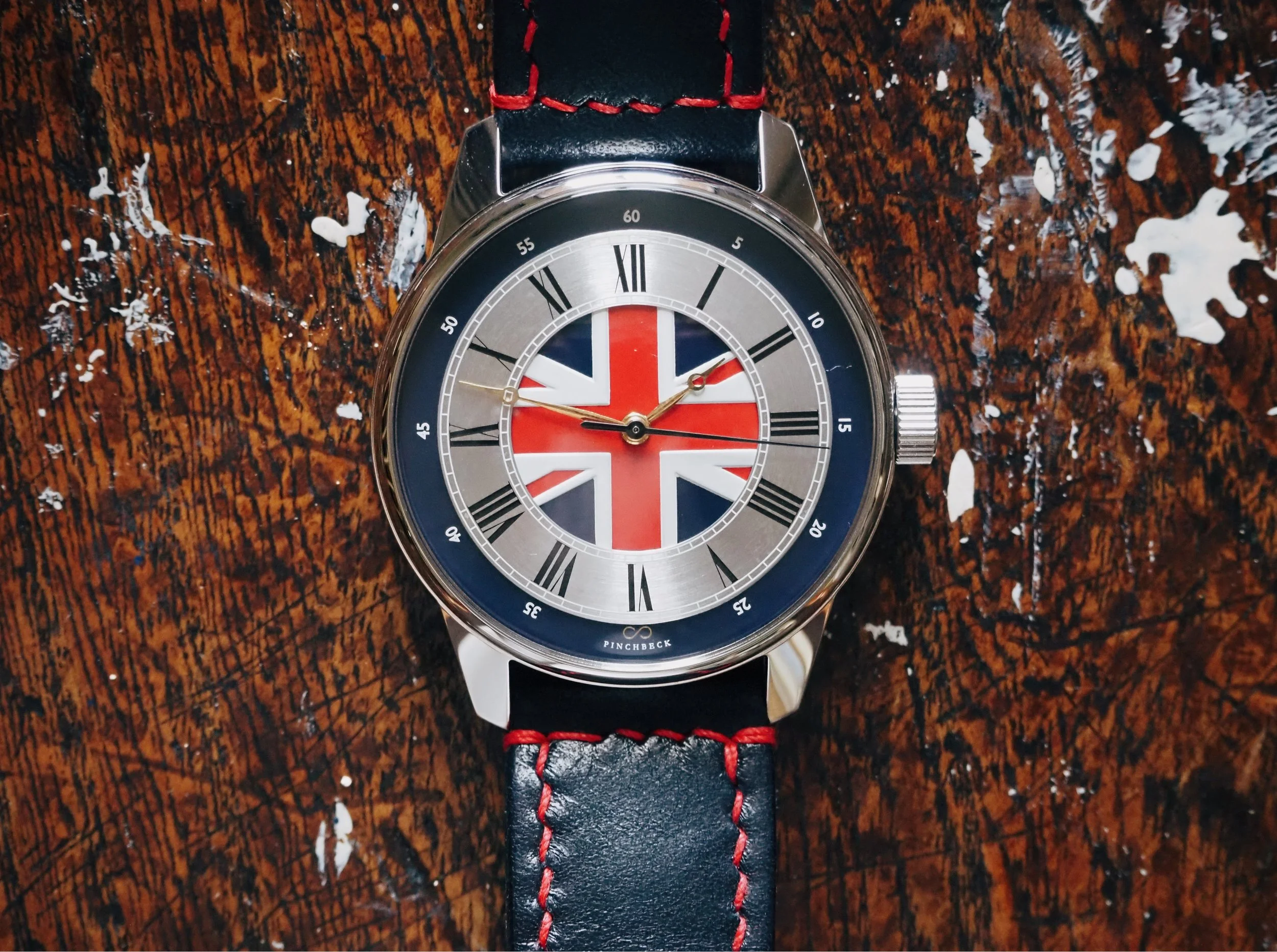 Watch with Union Jack flag face, Roman numerals, black and red leather strap.