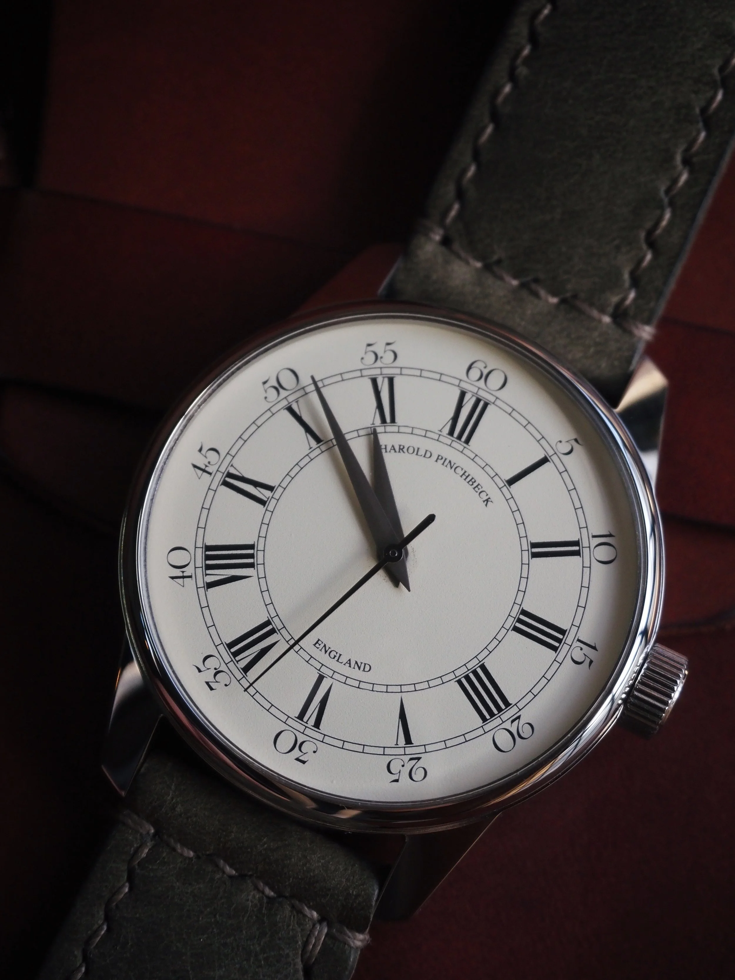 A wristwatch showing the time 10:48:50 with a white face, black Roman numerals, and a dark leather strap.