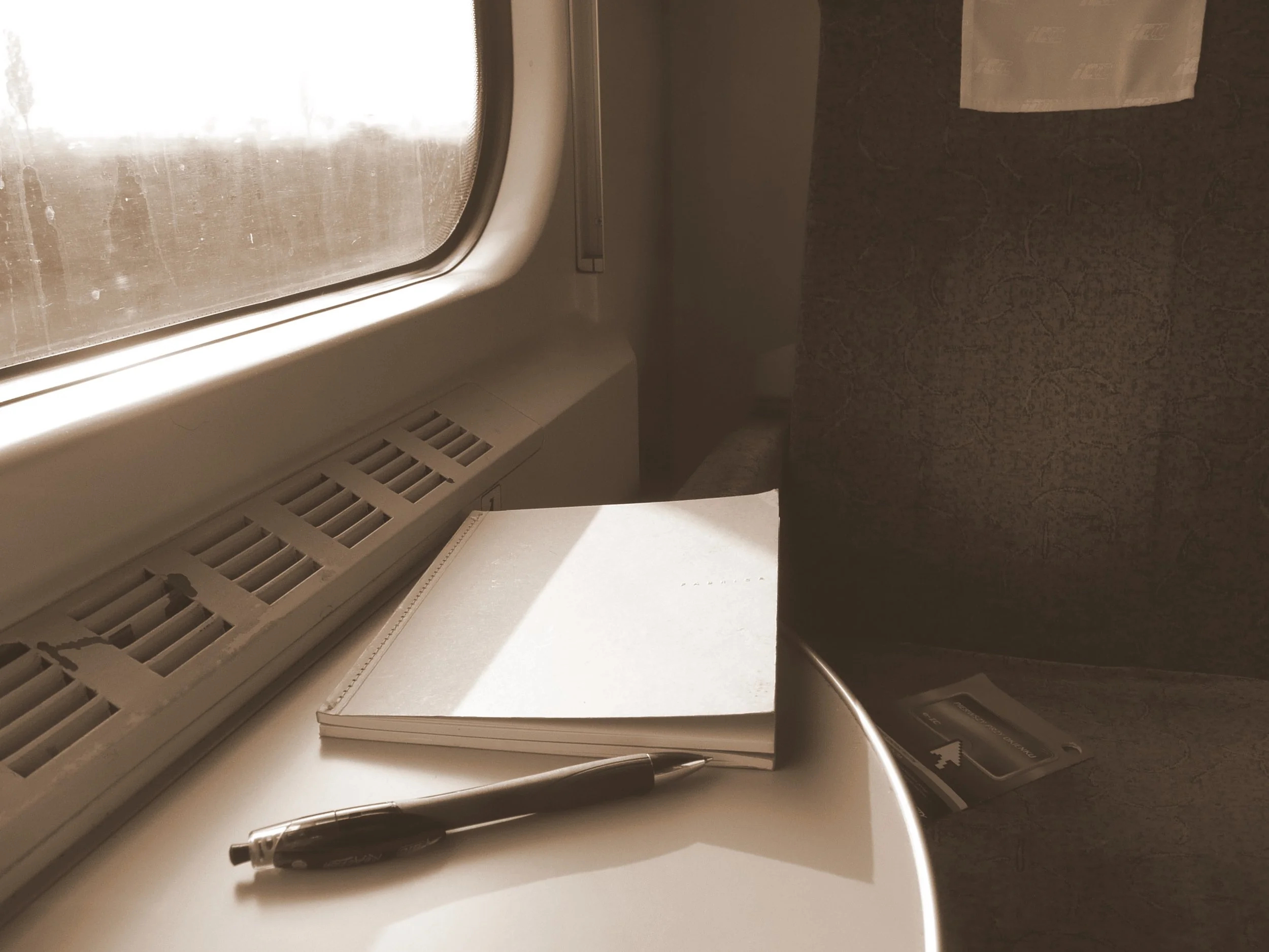 Pen and notebook sitting on a table on a train in sepia tone