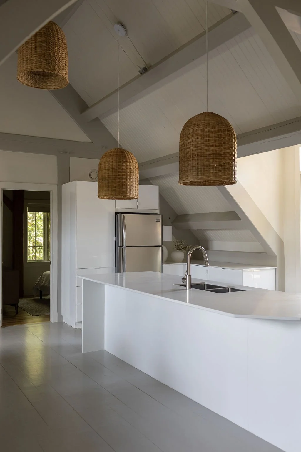 Second modern white kitchen with a white countertop, silver refrigerator, and three hanging wicker pendant lights.