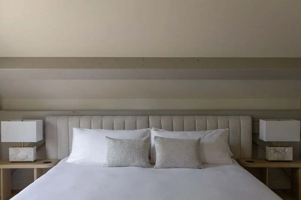 A luxury bed with neatly made white linens, gray pillows, and two lamps on wooden nightstands in a modern sophisticated bedroom.