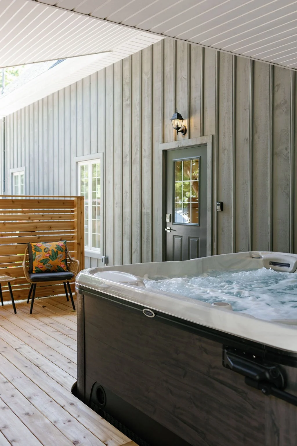 An outdoor patio featuring a private hot tub, lounge area, wooden flooring, and privacy panels.