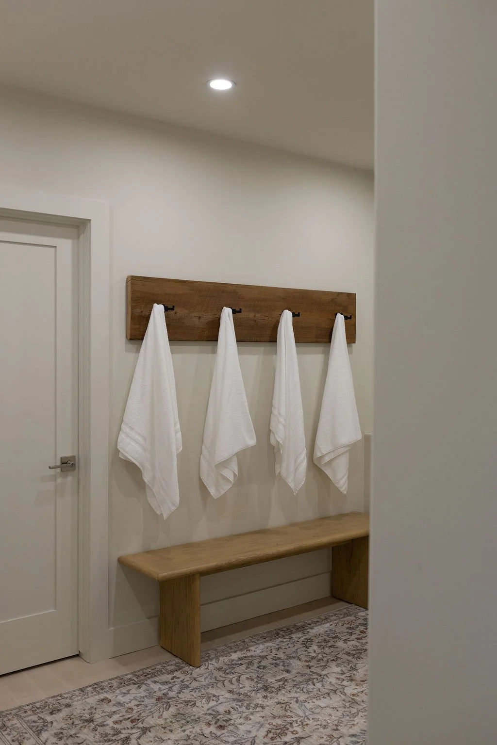 Entrance to the private spa with sauna and hot tub. A wooden coat rack with four hooks, each holding a fresh white towel, is mounted right as your exit to the spa. 