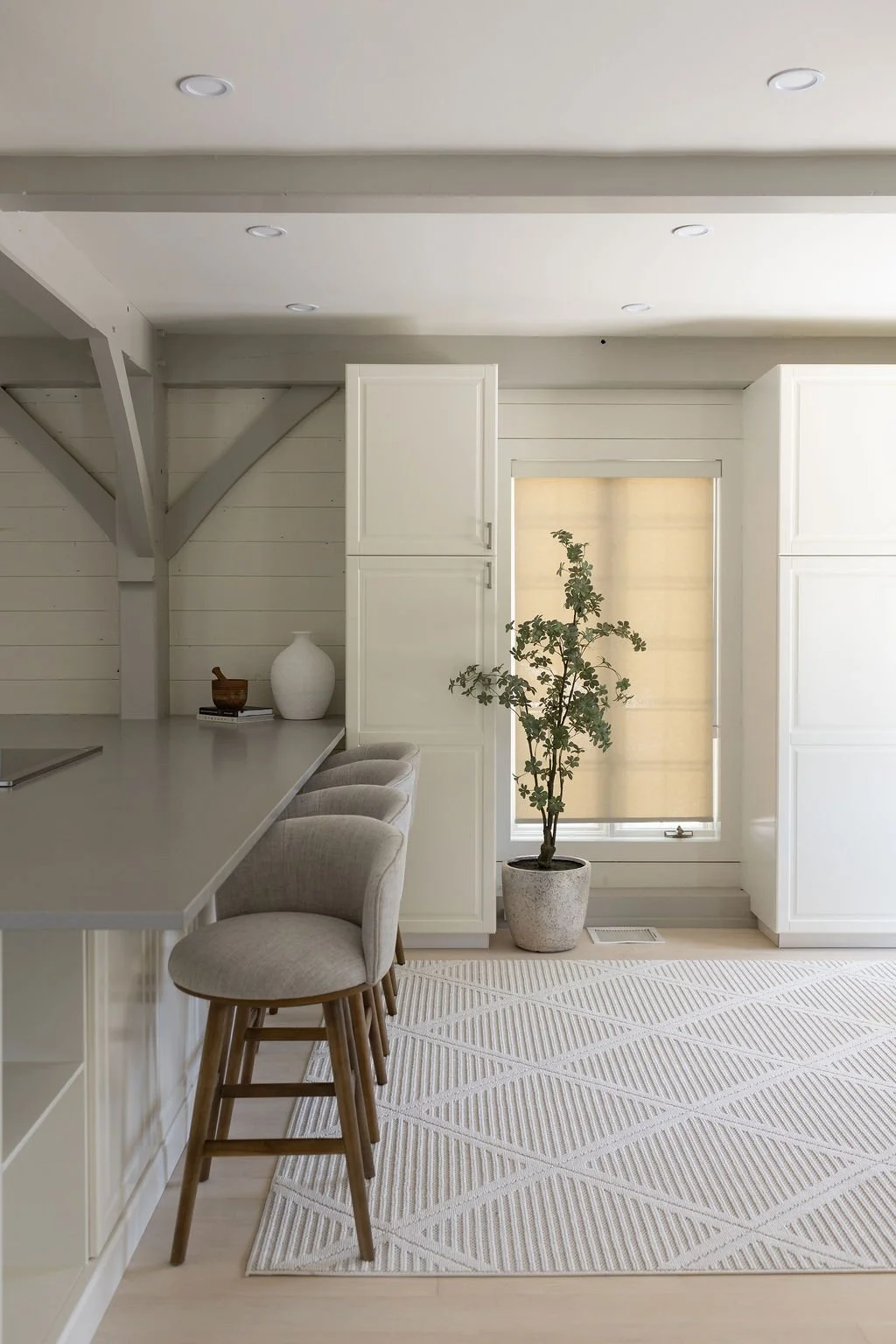 A modern chef inspired kitchen with white cabinets, a potted plant near a window, a white countertop and four bar stools.