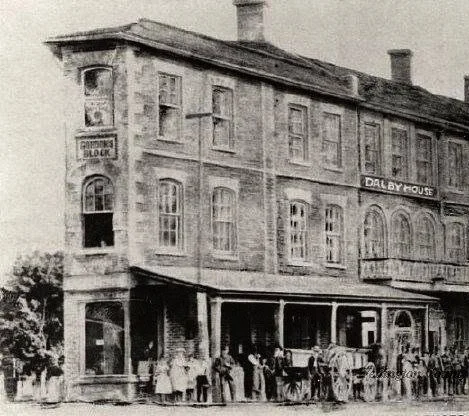 A black and white photo of an old multi-story building with a crowd of people standing in front. From the Ayrshire's history when it was referred to as the 'Dably House'.