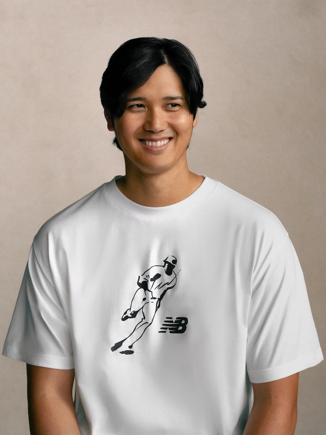 A young man with black hair smiling, wearing a white T-shirt with a black line drawing of a runner and the New Balance logo.