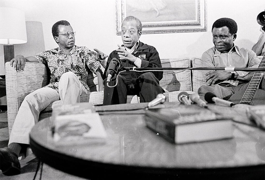 Three literary figures, from left to right: Nigerian novelist, poet + critic, Chinua Achebe; American novelist, essayist, playwright + orator, James Baldwin; Cameroonian writer, musician + composer, Francis Bebey. The photo was taken during the 1980 