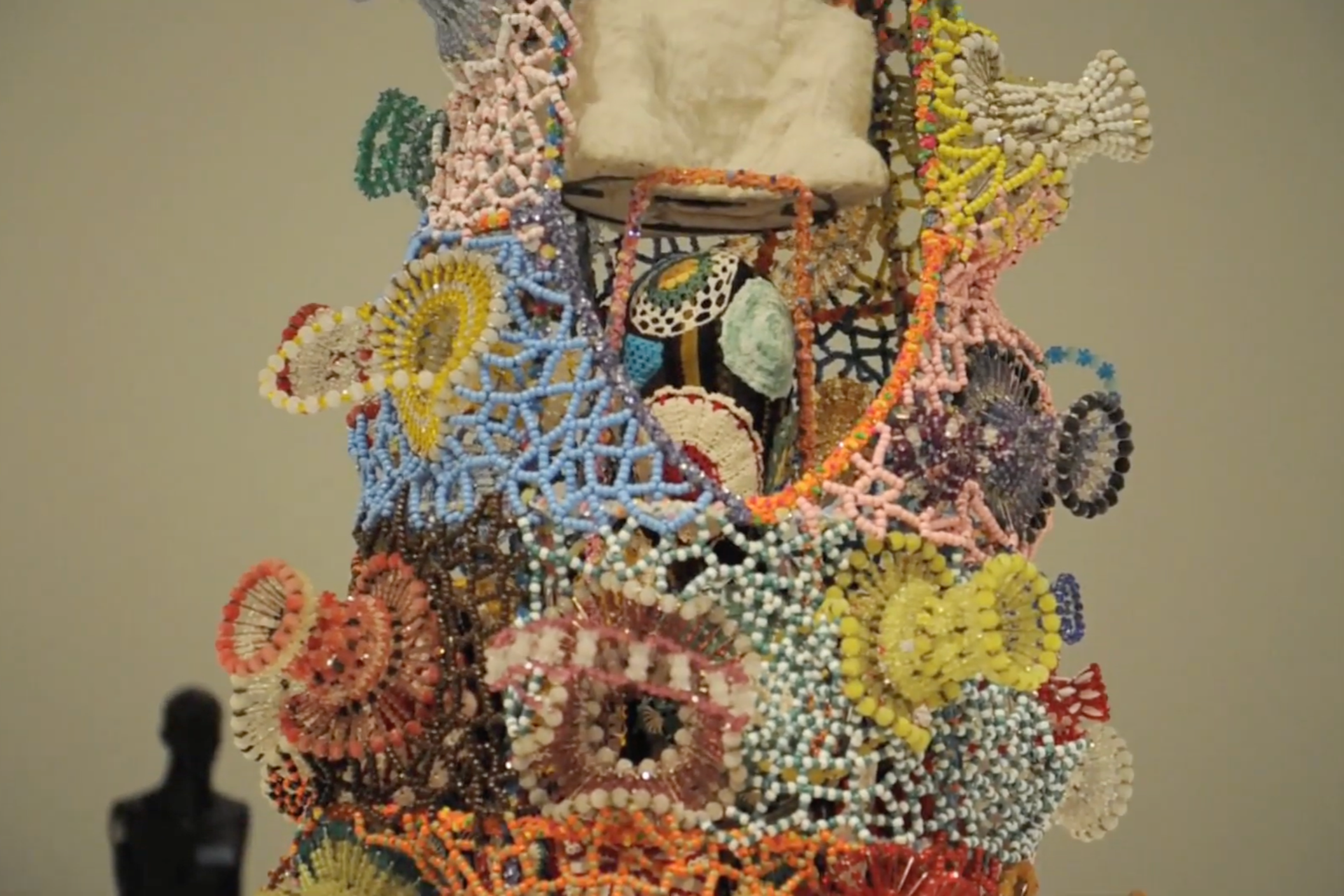 A detailed mosaic sculpture of a human face made from colorful beads, with various intricate patterns and a neutral background.