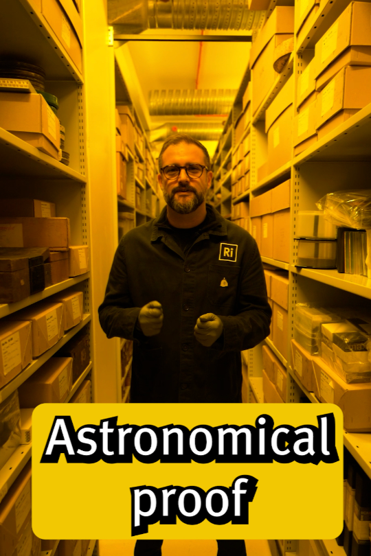 A man in a black jacket with an 'Ri' logo on it stands in an aisle filled with storage boxes, holding his fists in front of him in a confident pose, with the words 'Astronomical proof' overlayed at the bottom.