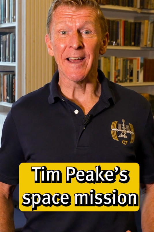 A man smiling, wearing a navy polo shirt with a logo, standing in front of a bookshelf, with a yellow text overlay that reads 'Tim Peake's space mission.'