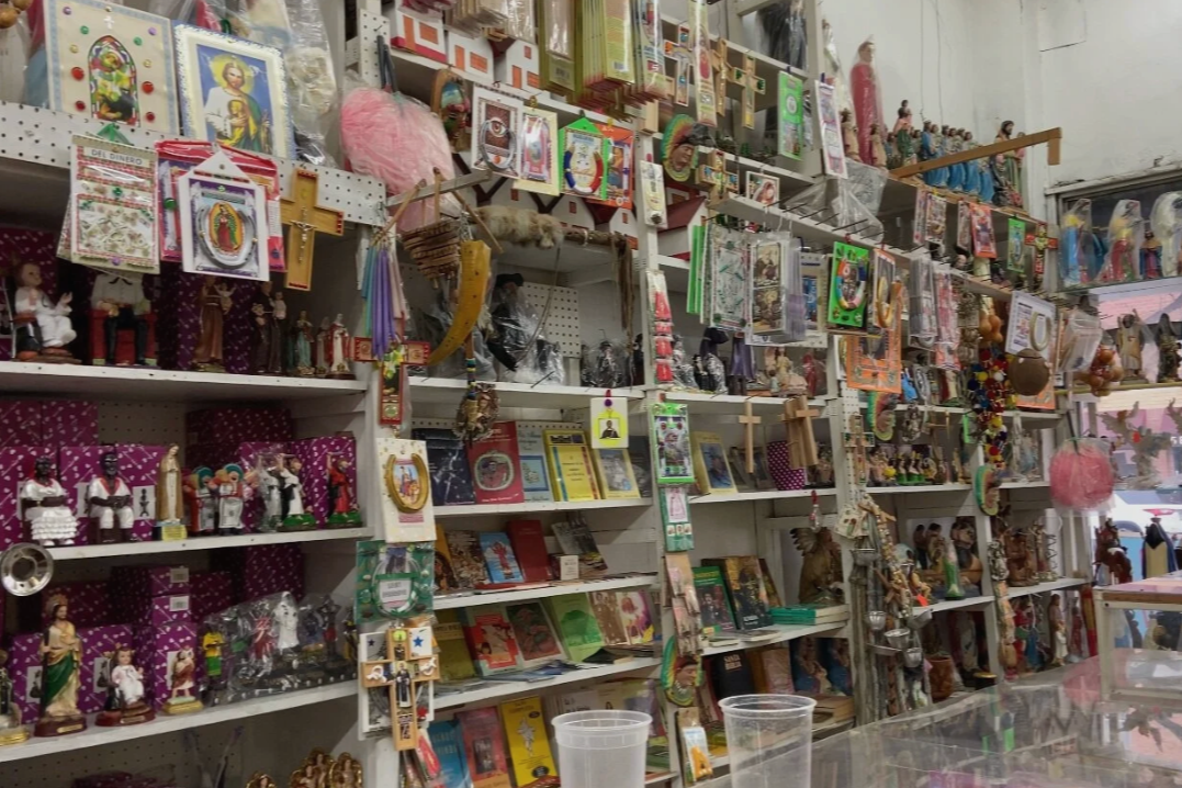 Shelves filled with religious figurines, books, and decorations in a gift shop, with a variety of Catholic saints and religious icons displayed.