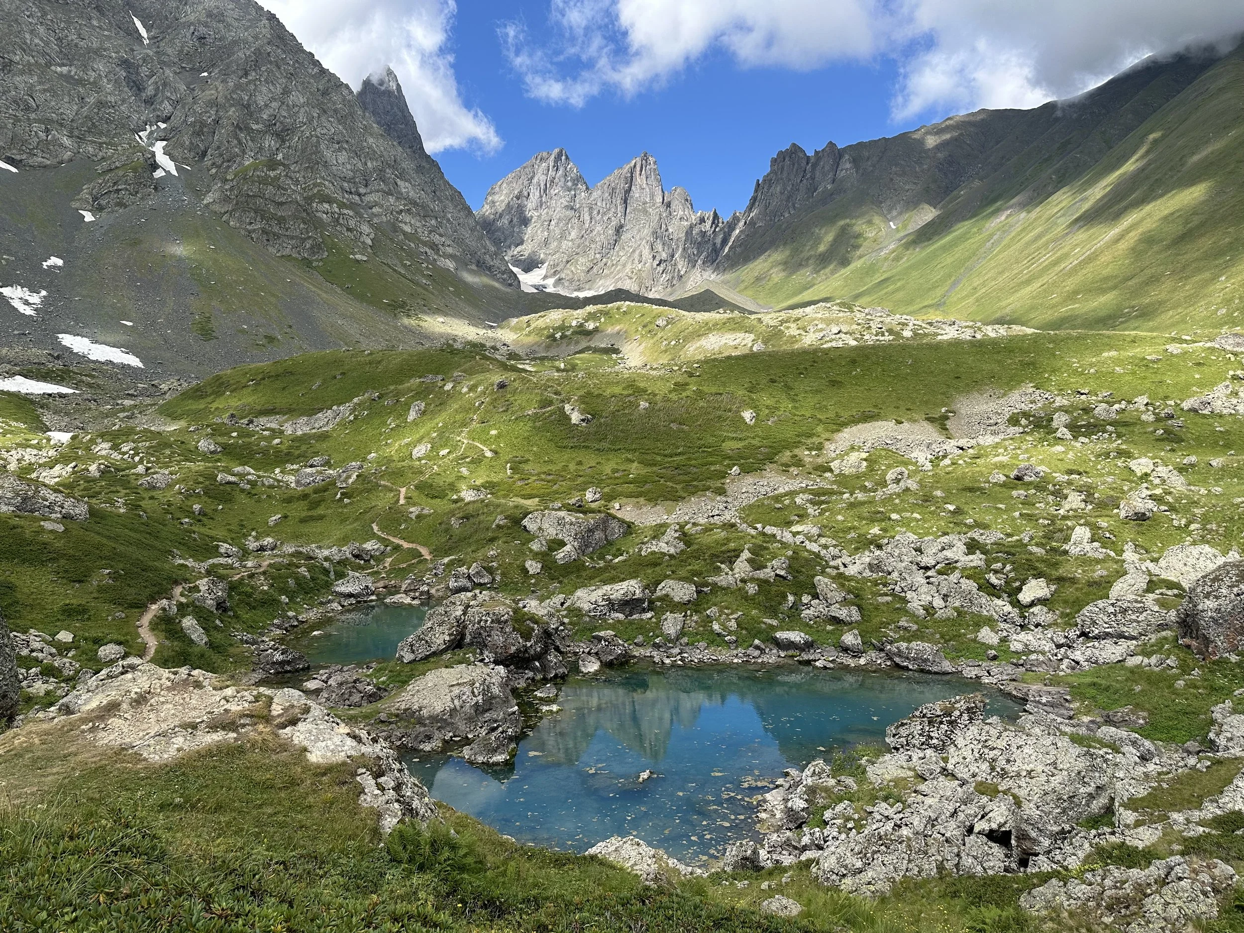 Abudelauri Blue lake surrounded by green alpine meadows, granite peaks, and blue sky