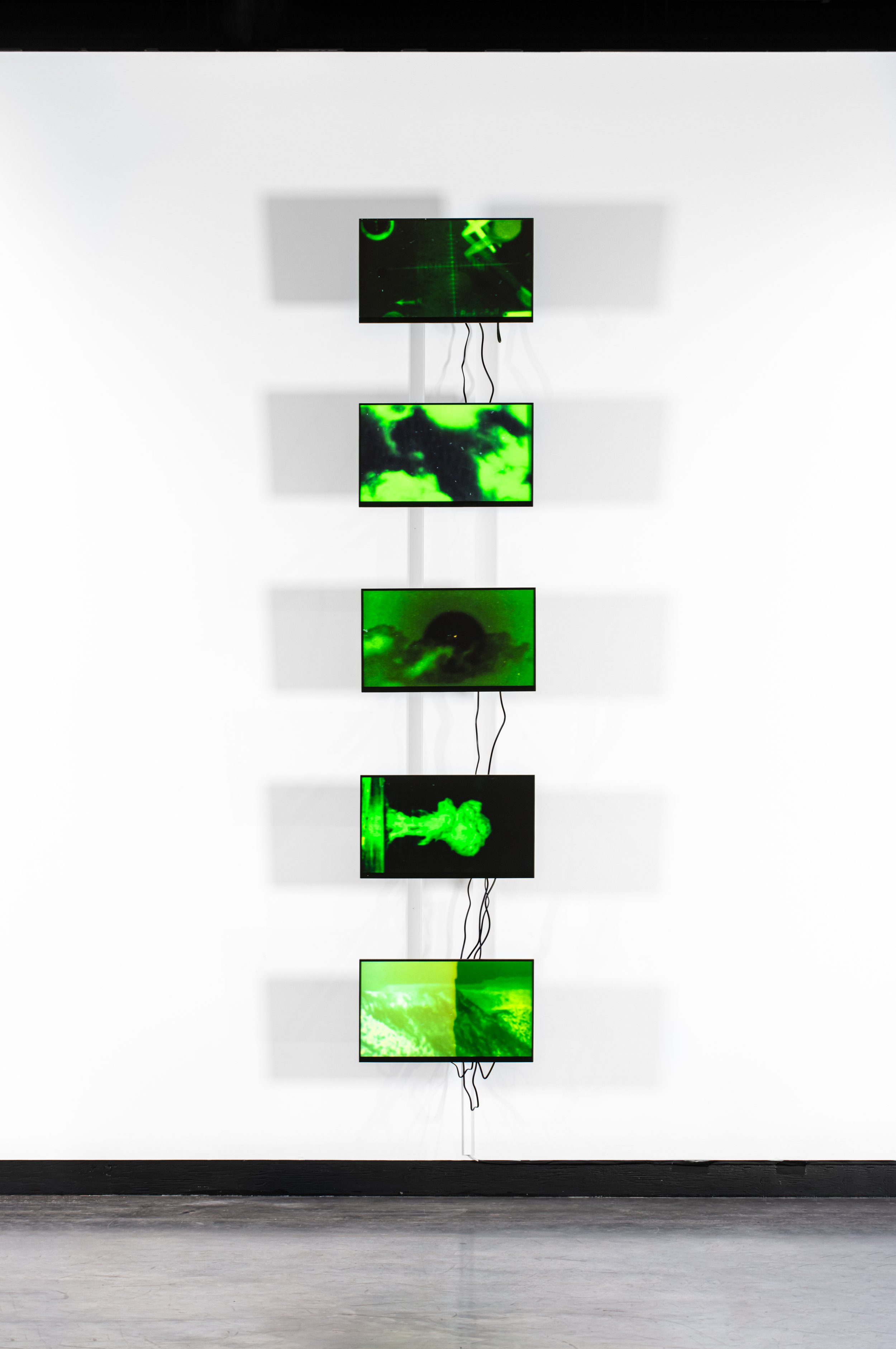  line of monitors playing green tinted videos of nuclear explosions. 