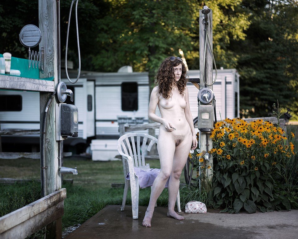  A nude woman standing in front of a camper. 