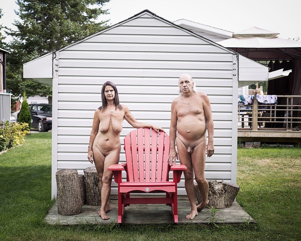  A nude couple standing next to a red chair. 