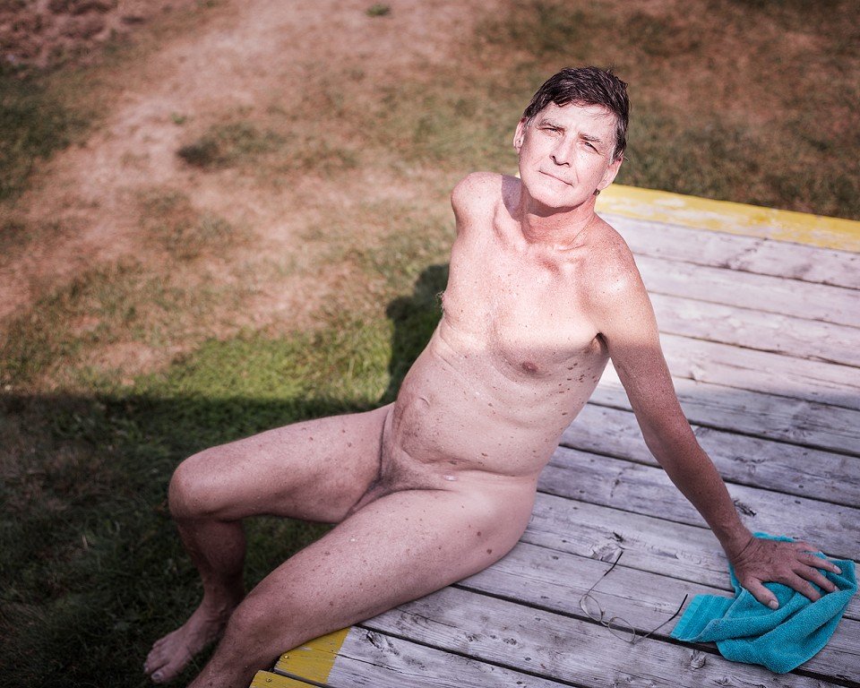 A nude man sitting on a wooden platform. 