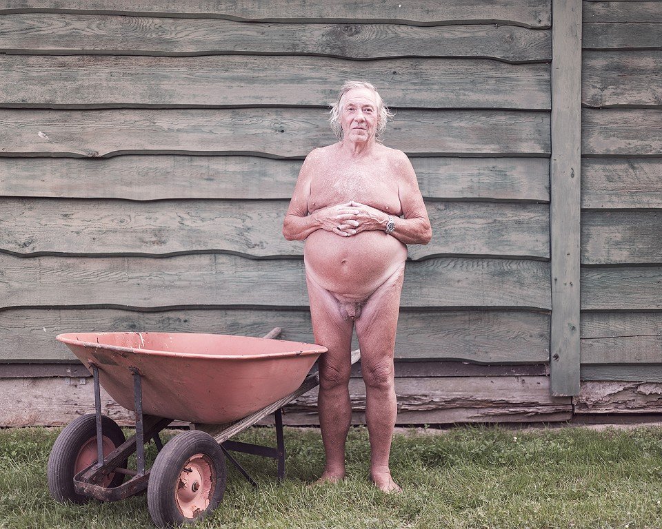  A nude man next to a wheelbarrow. 