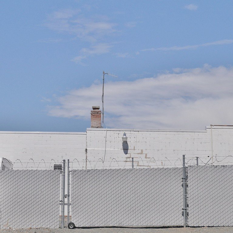  A barbed wire and blocked chain link fence in front of a white building. 