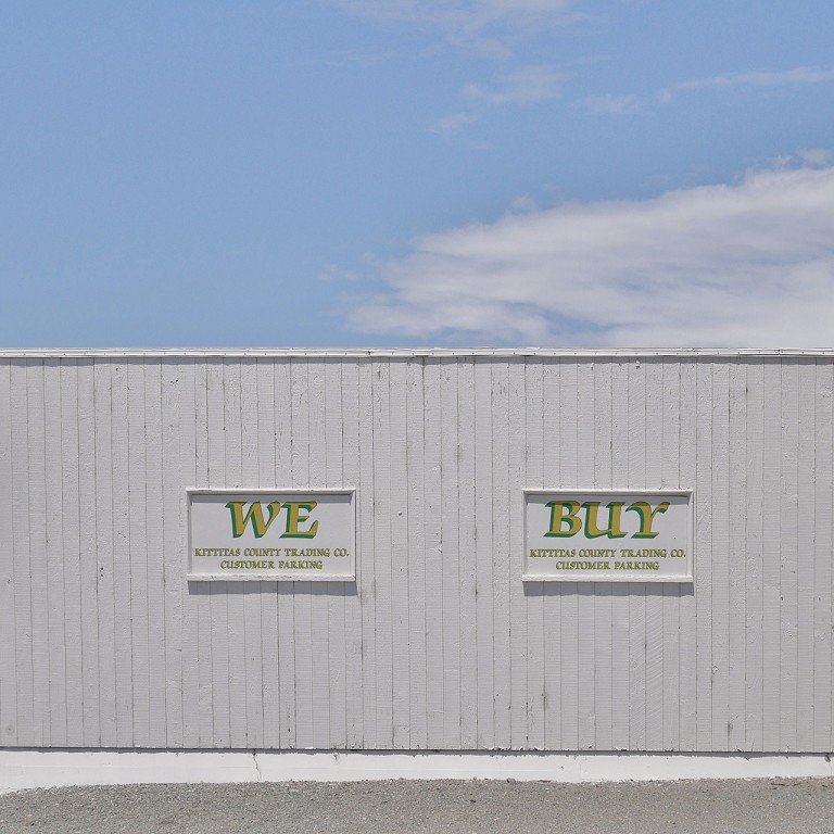  A white building with signs saying, “WE BUY.” 