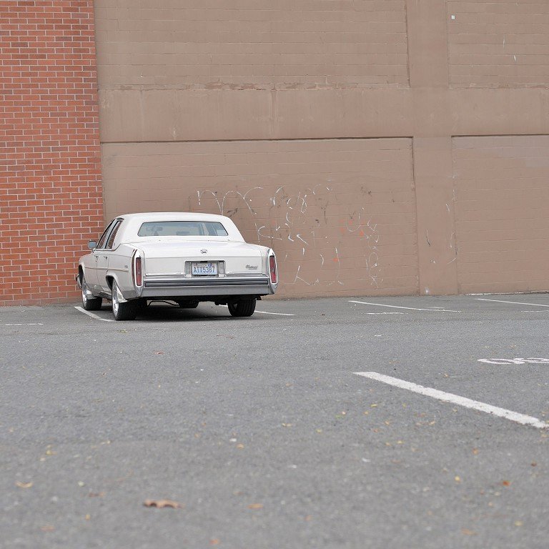  A white car parked in front of a brick building. 