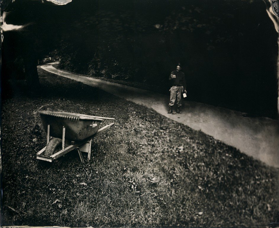  A black and white photo of a person on a trail and a wheel barrow. 