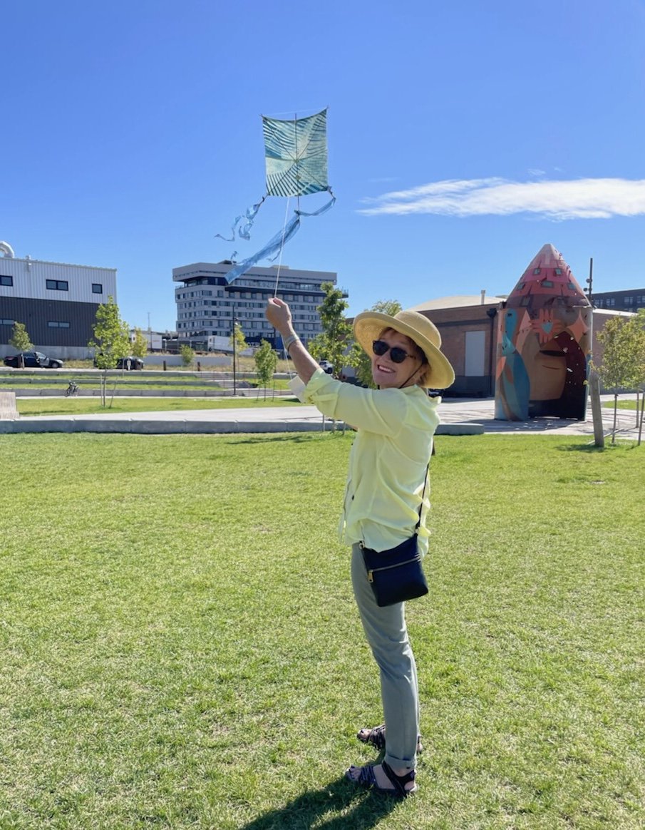  Woman flies her kite. Looks back towards the camera. 