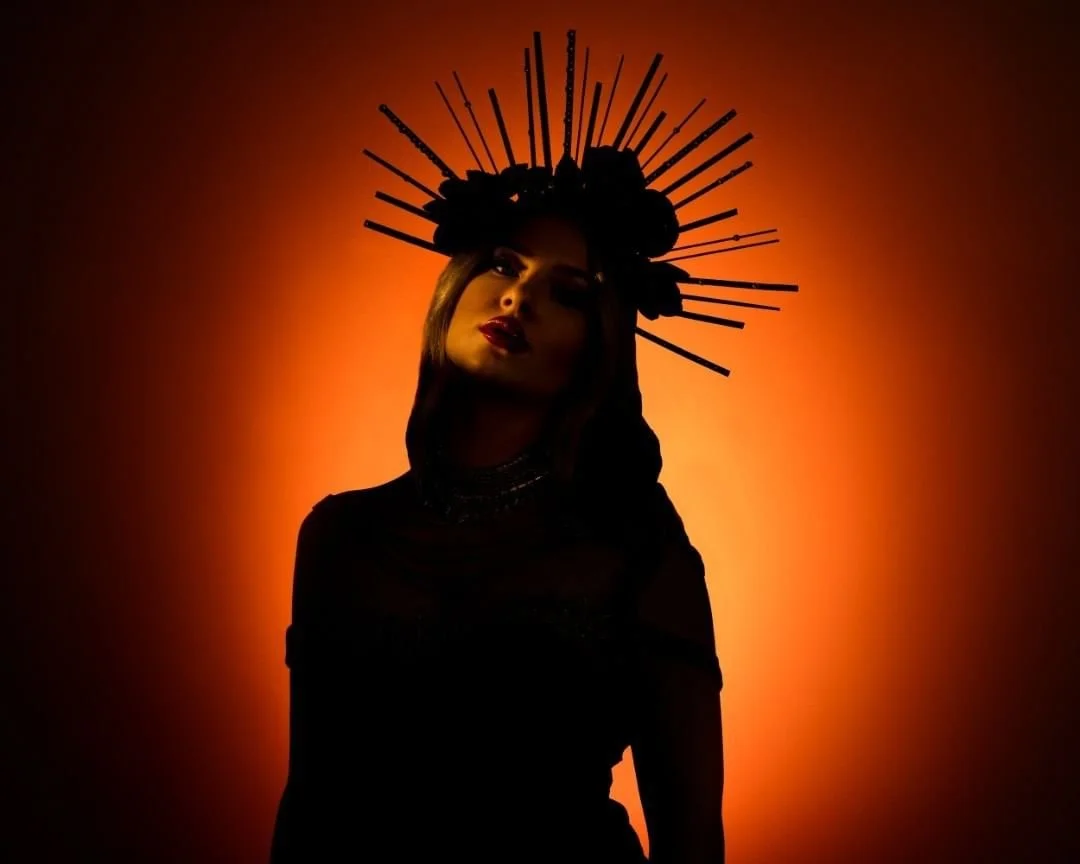 A woman wearing a black outfit and a dramatic jewelry necklace, with dark makeup and lipstick, is shown in front of a warm orange background. Album Art for Dani Kristina, Burning Parachute.
