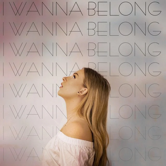 A young artist, Dani Kristina, with long blonde hair looking upward against a background with repeated text that reads 'I WANNA BELONG'.