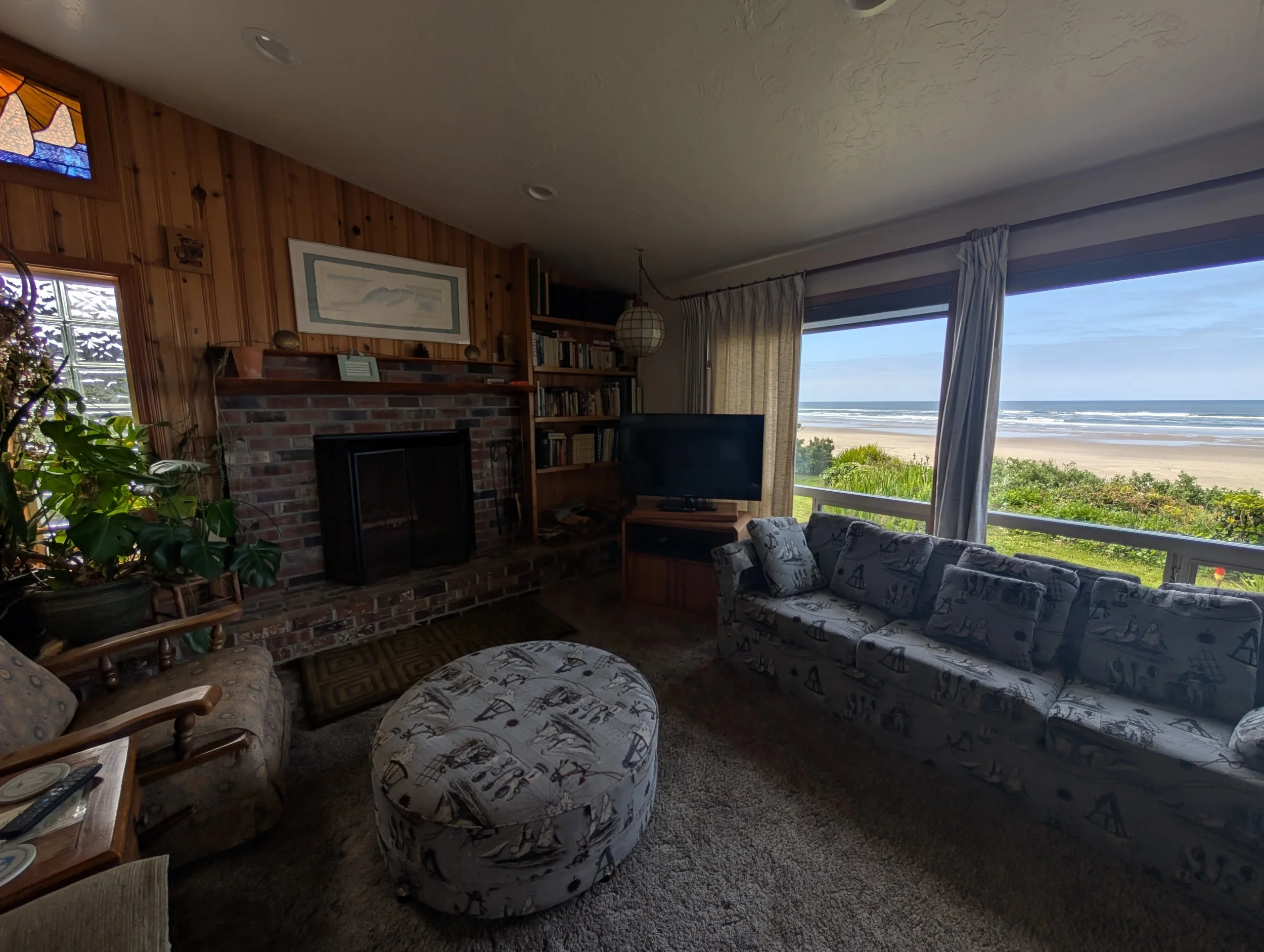 Living room with furniture and a large window showing a beach view.