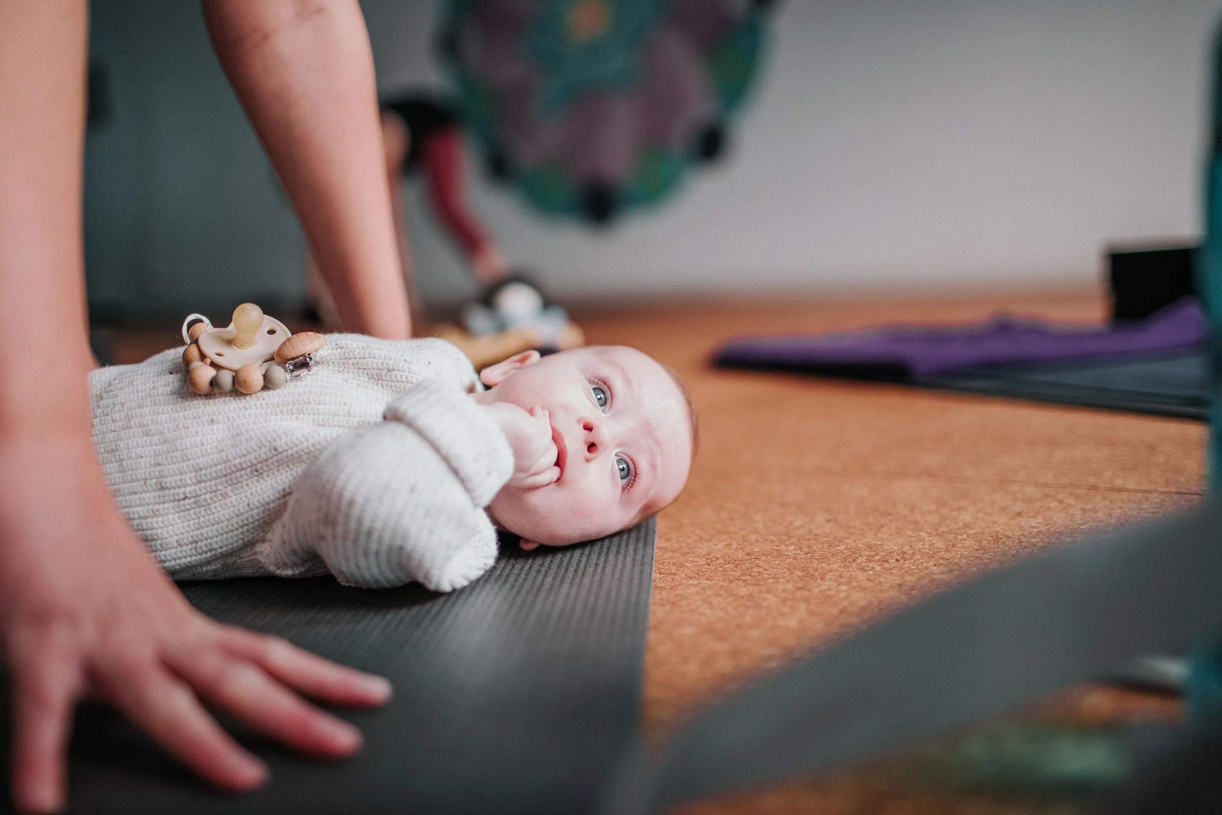 baby laying on a yoga mat while mum practices yoga in a postnatal class for mums and their babies at bloom yoga perth