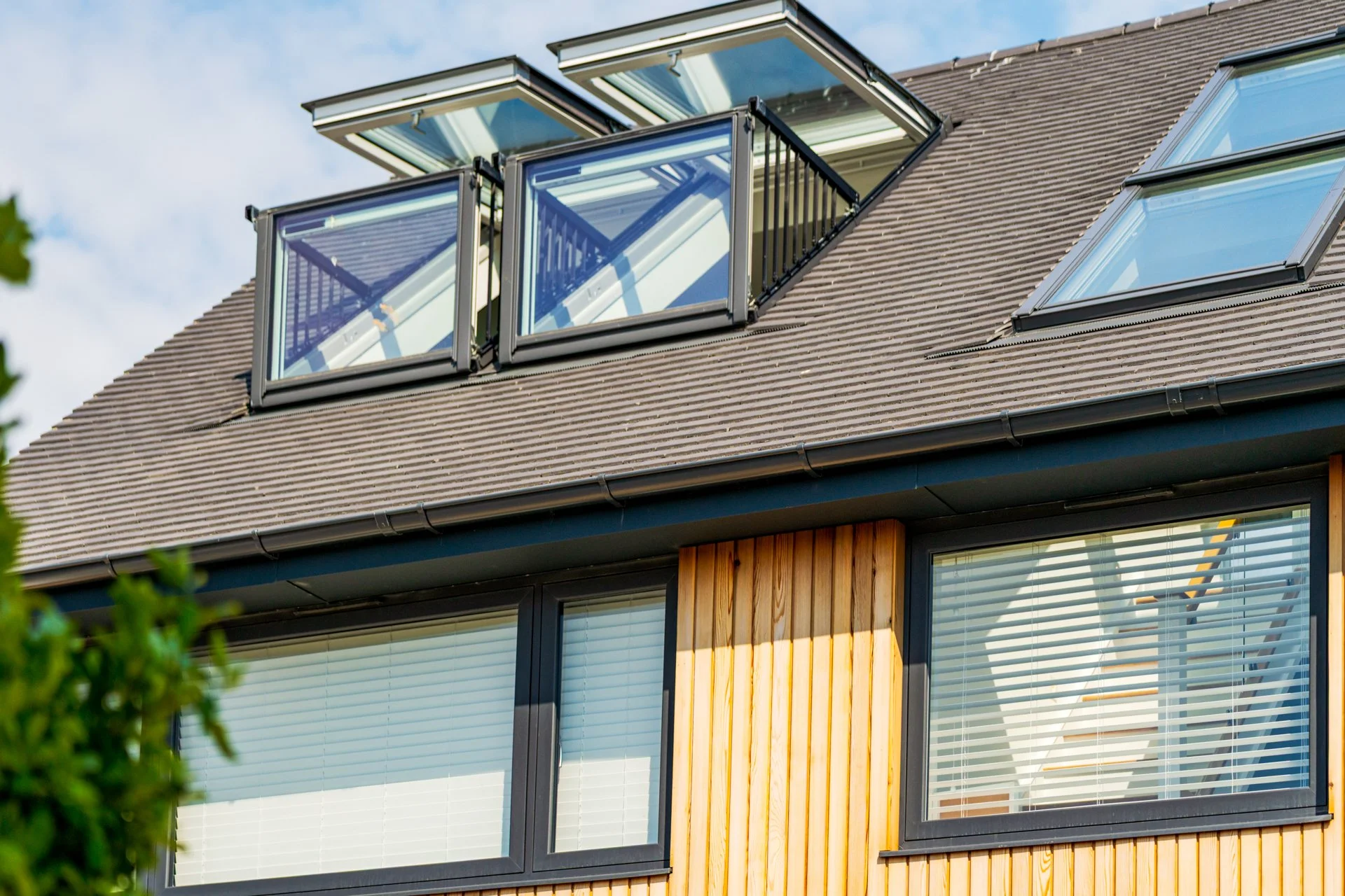 Close-up of a modern house window with a wooden exterior and a tiled roof with multiple skylights and solar windows.