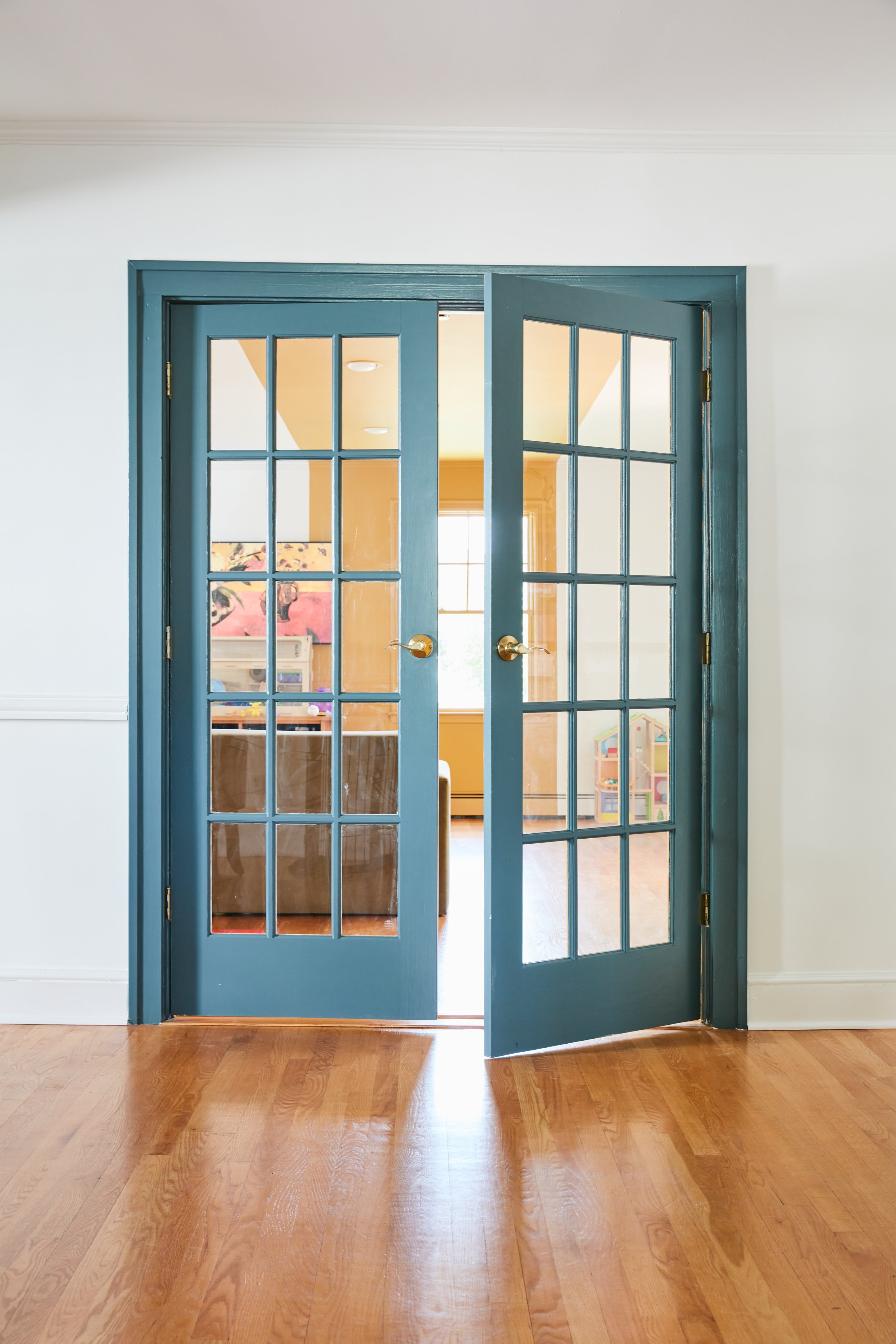Double french doors painted in Farrow and Ball Inchyra Blue opening into the family room. The walls are painted in Benjamin Moore Simply White