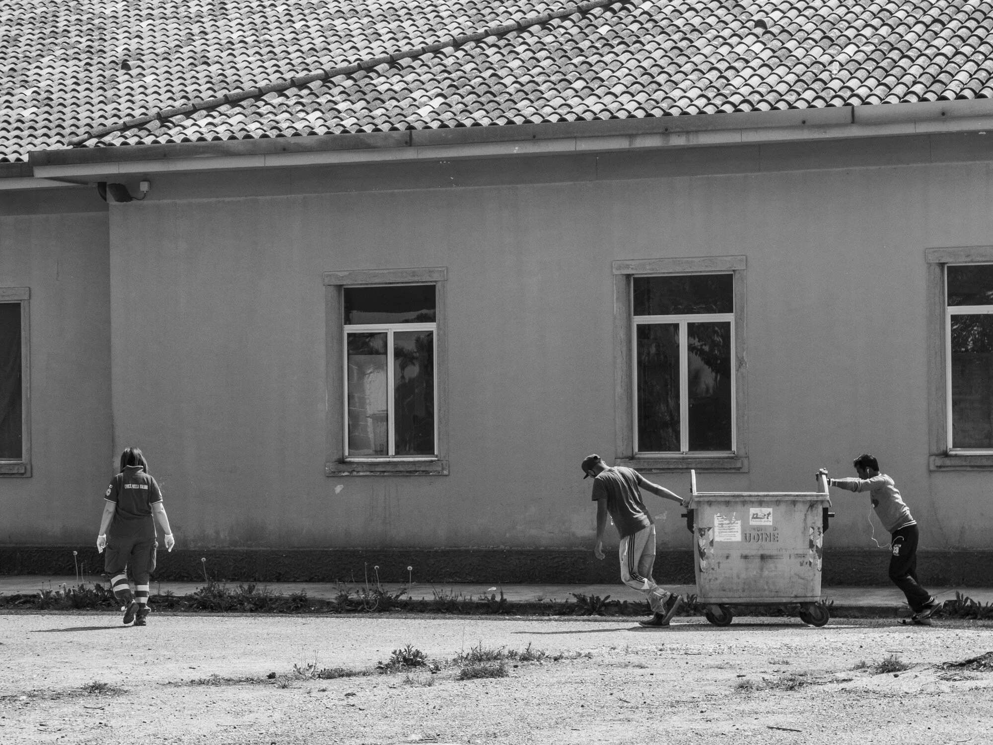   Red Cross Camp   Migrants are seen with a red cross worker at a refugee camp in Bologna, pushing a skip bin. Camps managed by organisations like the red cross are completely full and lack funding, causing many people to remain on the streets until 