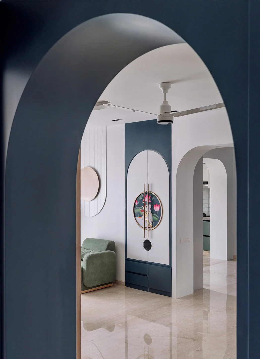 Interior view of a modern living space through an arched doorway with a ceiling fan, minimalist artwork on the walls, a green armchair, and decorative accents.