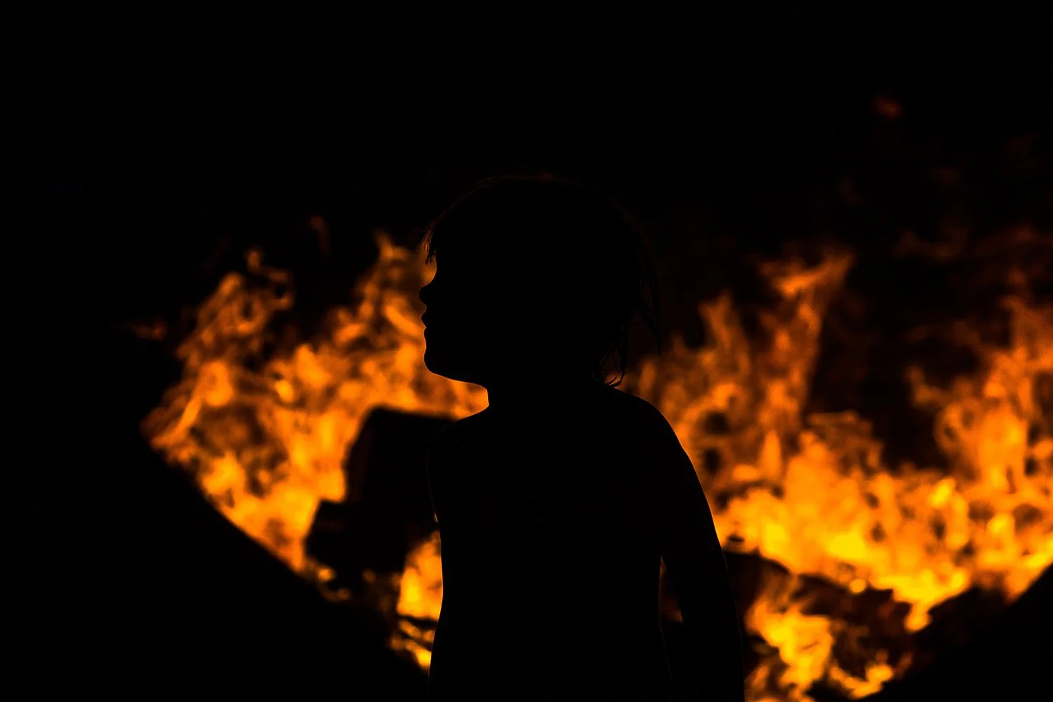 silhouette of little boy playing around campfire at night