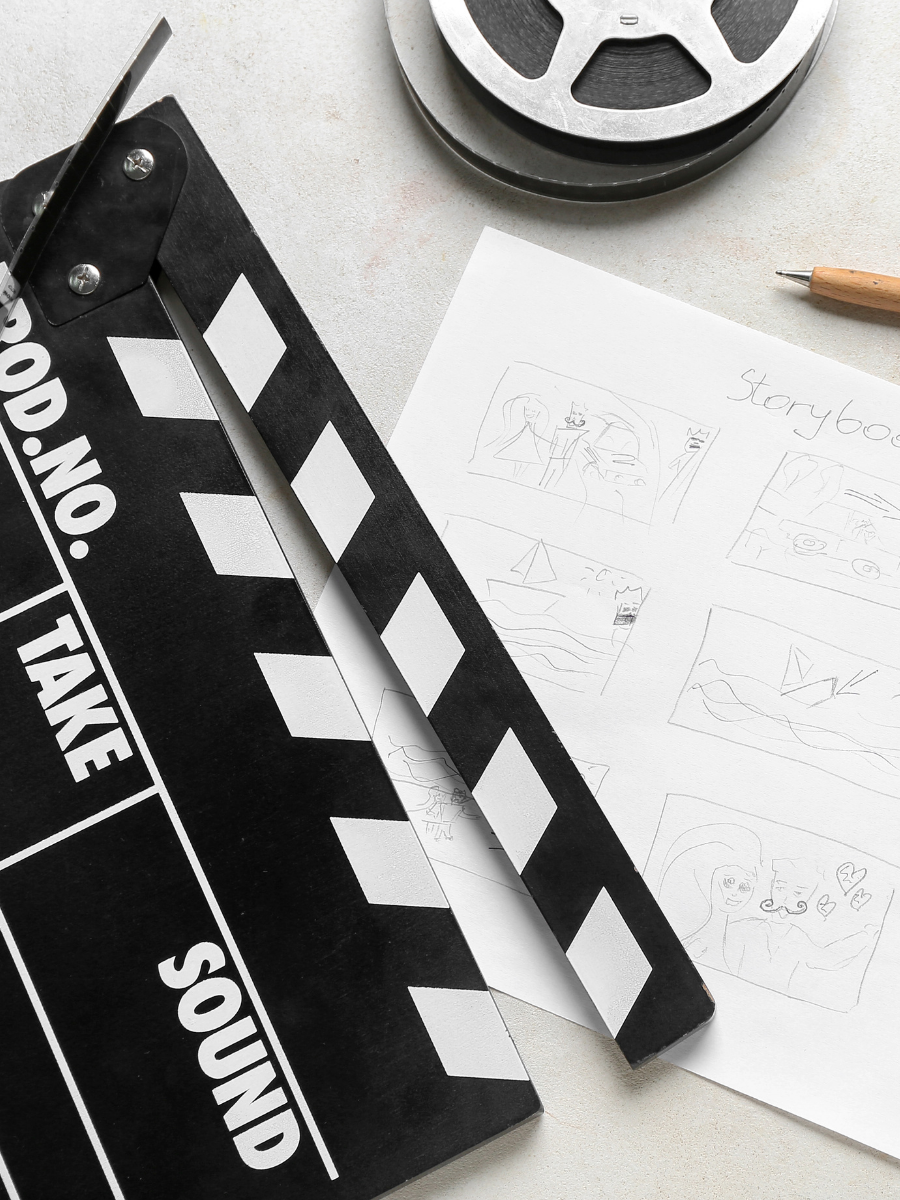 A film slate, a piece of paper with sketches and the word 'Storybook' written, a wooden pen, and a film reel on a light-colored surface.