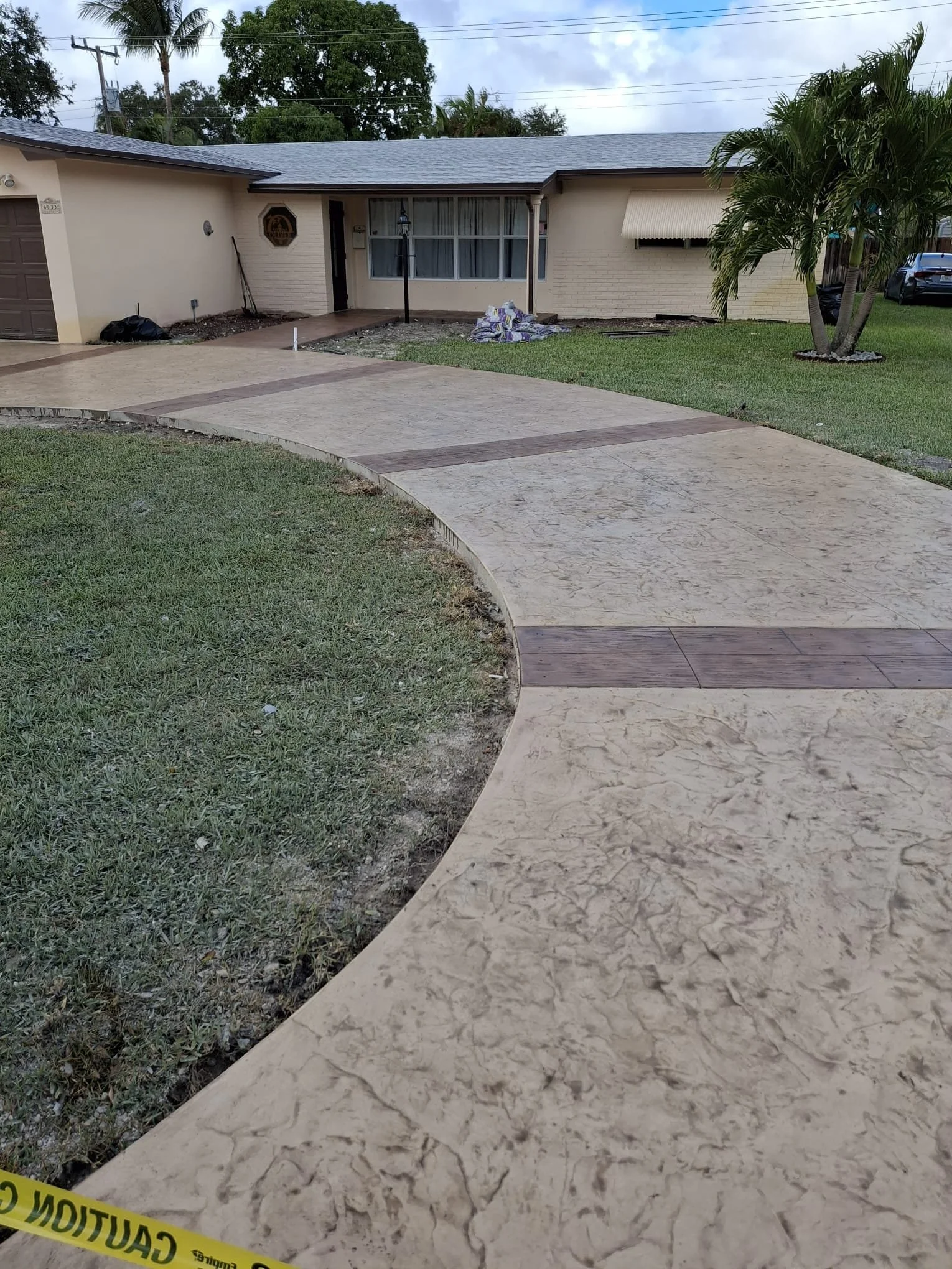 Front view of a single-story house with a wide decorative stamped driveway and colored ribbons of art throughout the driveway.