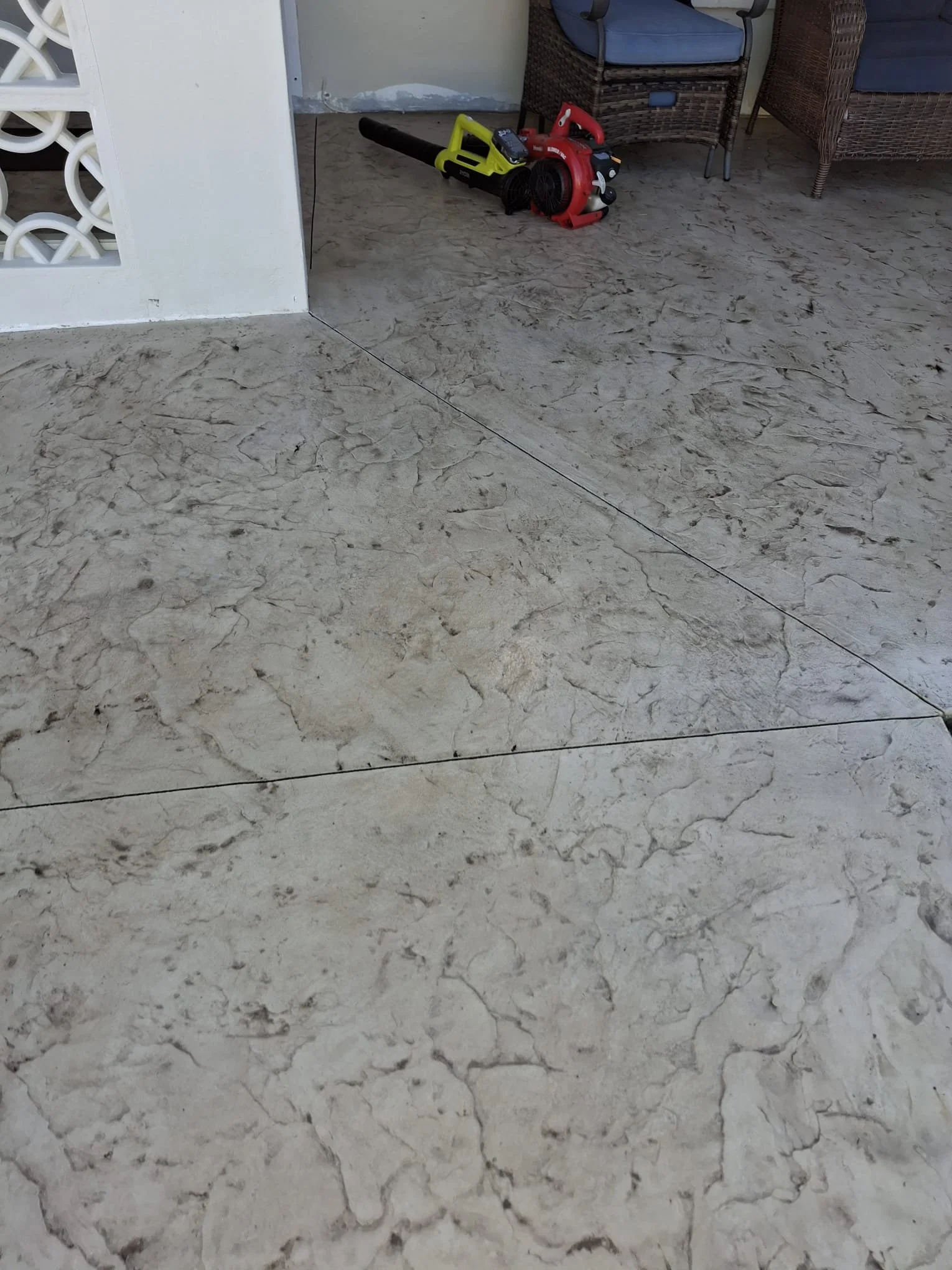 Textured patio flooring with outdoor furniture and a leaf blower in the corner.