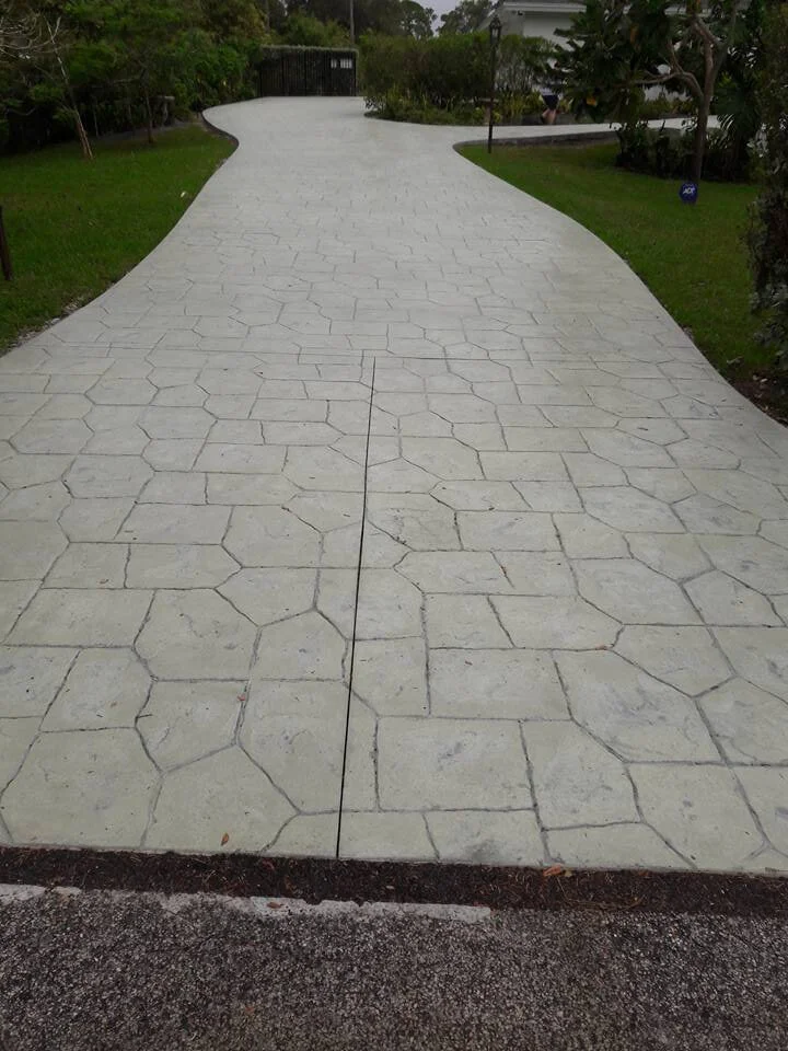Stamped concrete driveway with hexagonal pattern surrounded by grass and trees.