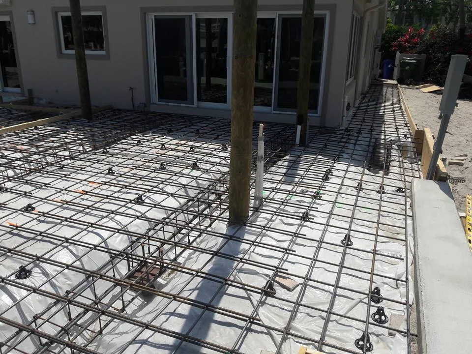 Concrete slab preparation with rebar and wooden posts at a construction site next to a building.