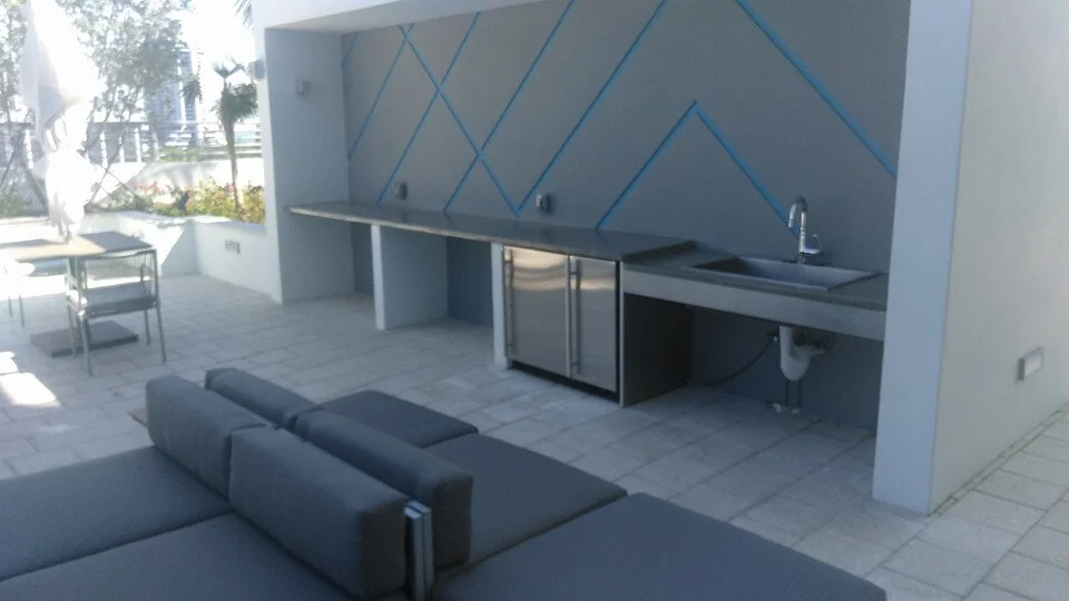 Modern outdoor kitchen with concrete countertop, built-in sink, and geometric wall design