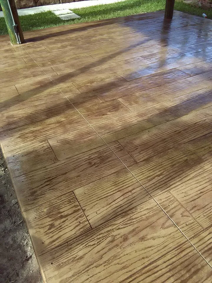 Stamped concrete patio with wood grain texture and grass border.