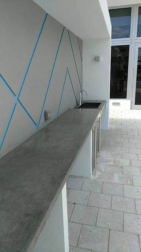 Modern outdoor kitchen with concrete countertop, built-in sink, and geometric wall design.