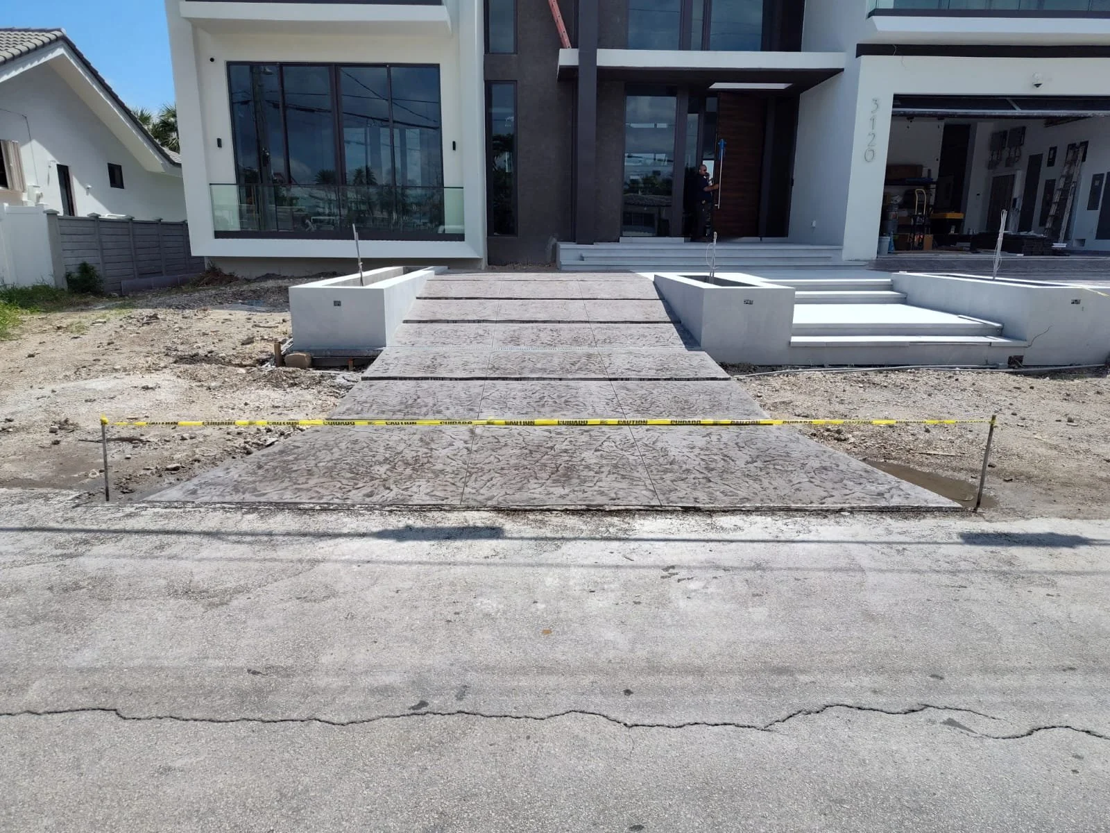 Modern house with new concrete driveway under construction, caution tape barriers, and front steps.