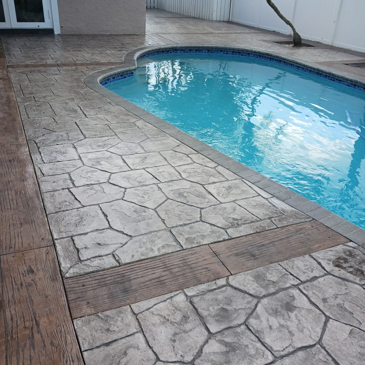 Swimming pool with stamped decorative concrete patio showcasing stone and wood textured deck.