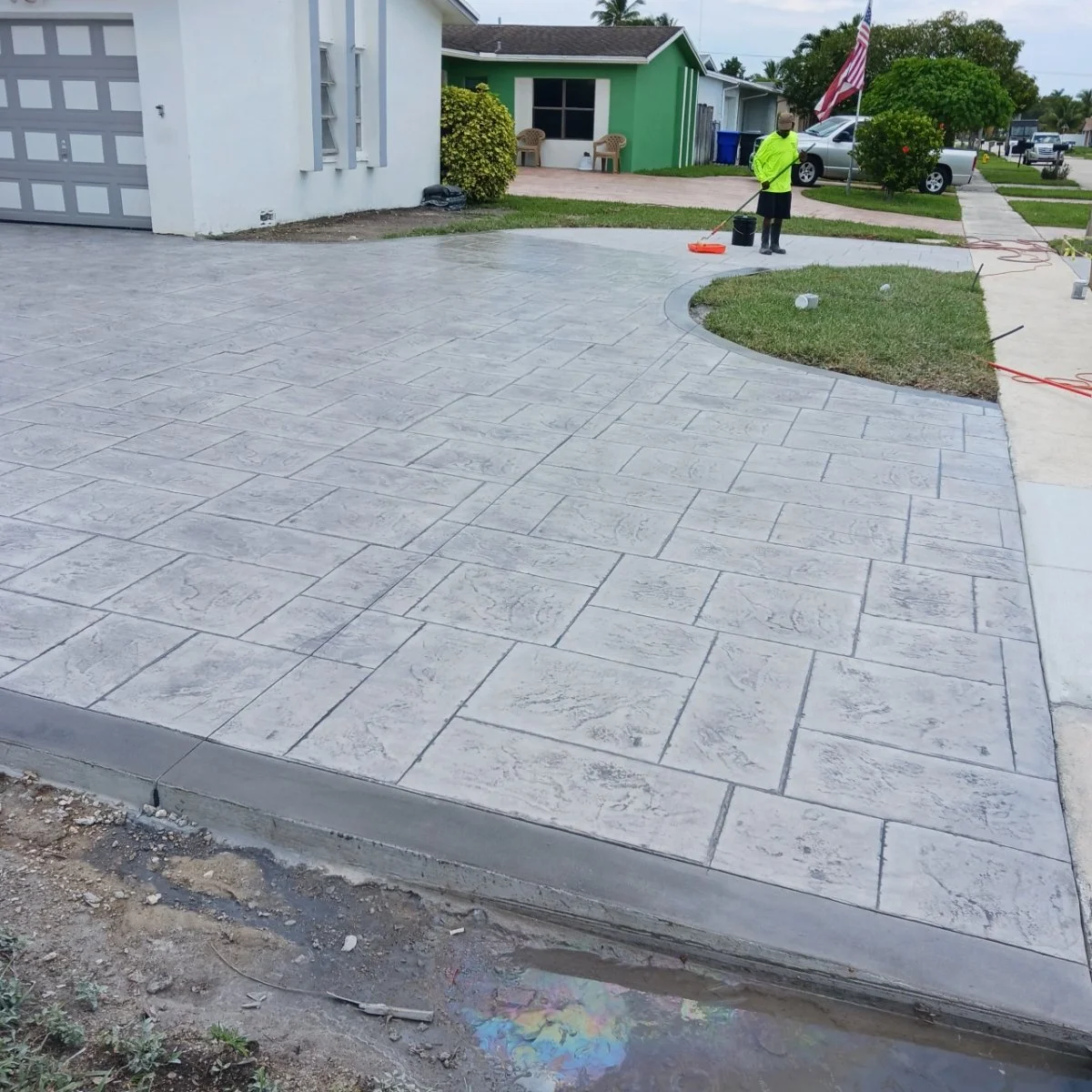 Freshly paved concrete driveway with stamped pattern, person cleaning surface, suburban residential setting.