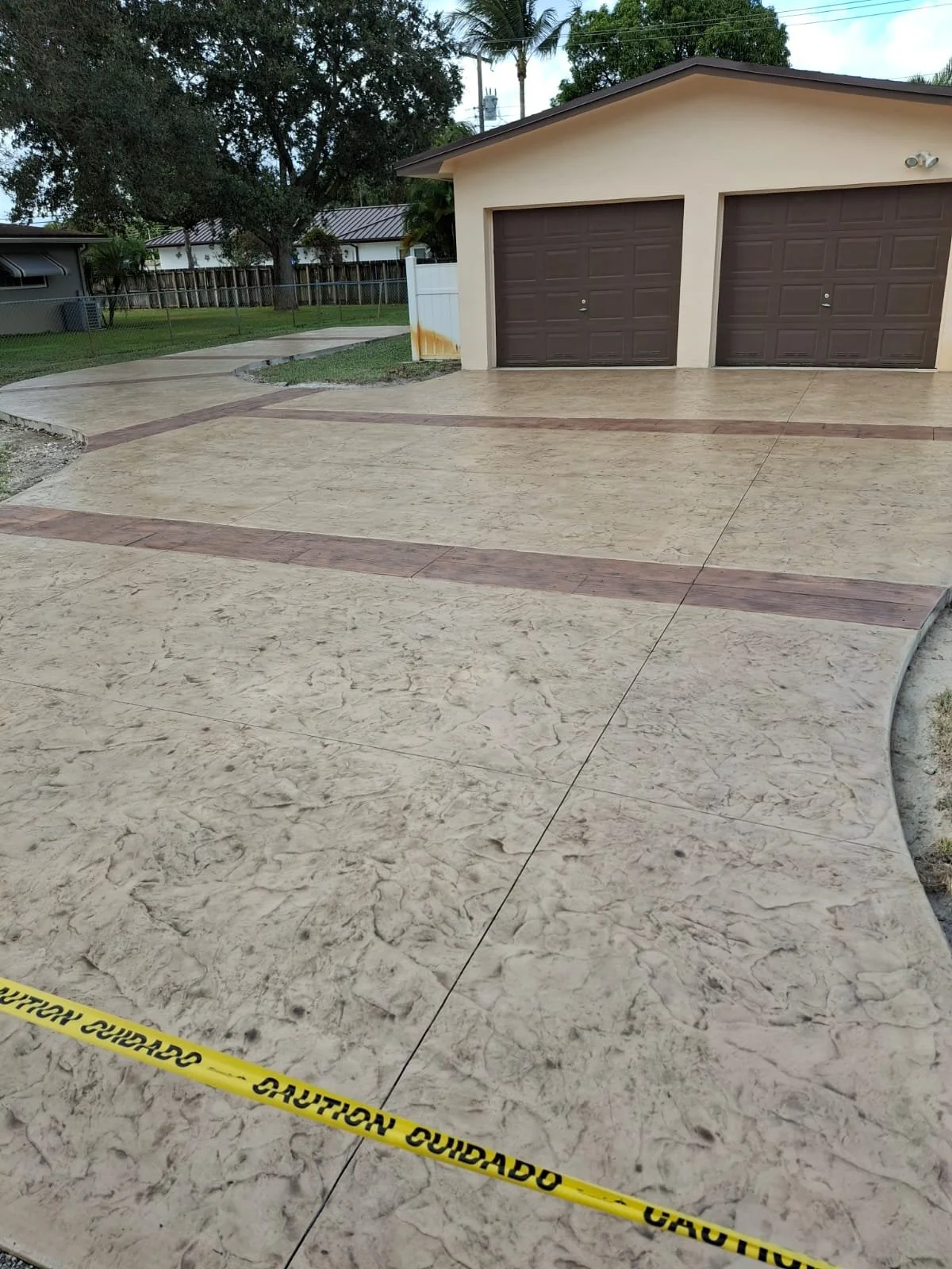 Garage with two brown doors and newly paved decorative stamped concrete driveway with colored textured ribbons throughout.