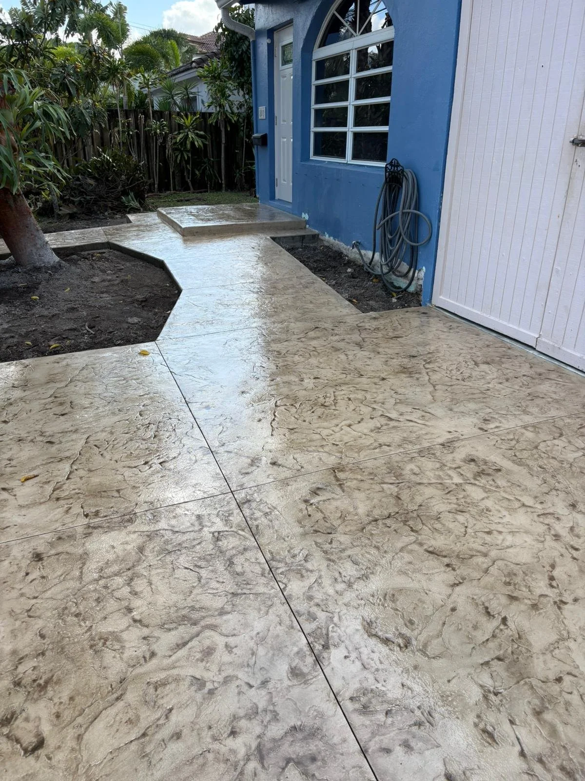 Colored, decorative Stamped concrete pathway leading to a blue house.