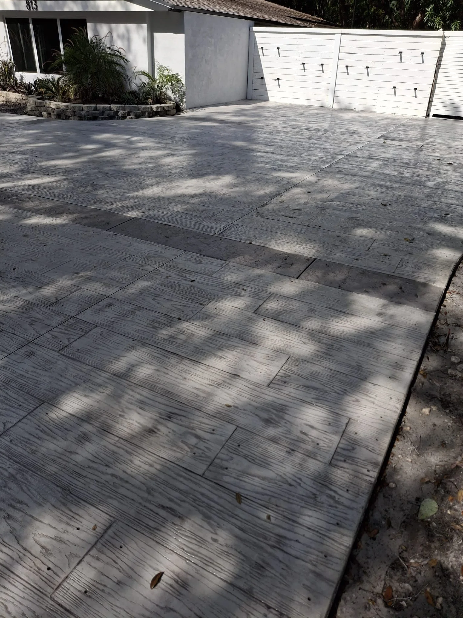 Decorative Stamped Concrete driveway with wood-like texture near a white house with garage doors.